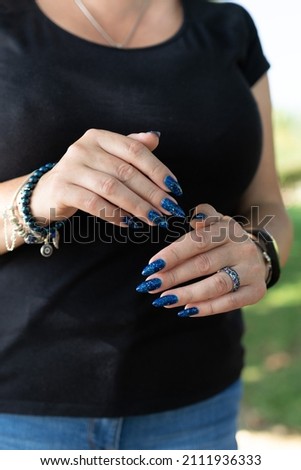 Woman's beautiful hand with long nails and blue manicure with bottles of nail polish	