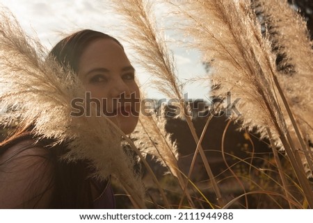 Caucasian woman's face peeks out between golden foxtail flower in golden toned autumn setting outside in meadow in Mexico