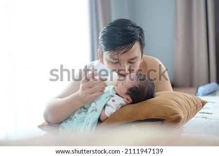 Soft focus. Young father kiss his newborn baby during feeding milk at home. 