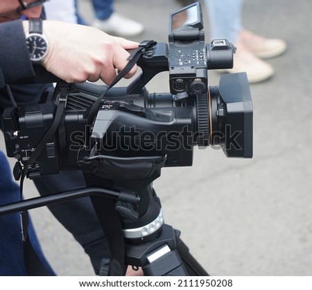 young camera man and video operator doing reportage with his professional camera on tripod at street. man journalist, operator and reporter with video camera on tripod filming action on the street 
