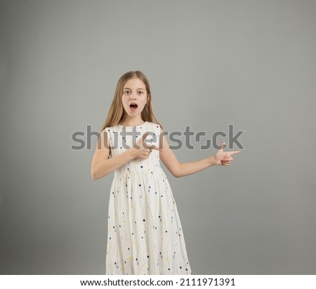 a young girl in a light dress points her fingers to the side with a smile on her face on a gray isolated background.