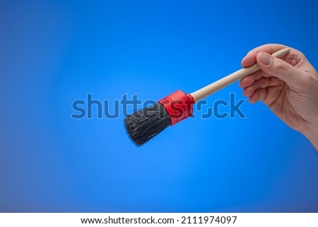 Dusting brush with wooden handle held by male hand. Close up studio shot, isolated on blue background.