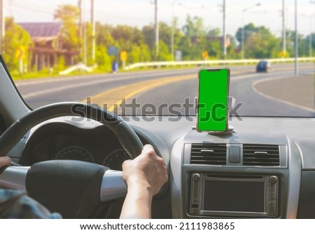 Car driver driving on curve road and using GPS map navigation application on smartphone, blank green screen smartphone