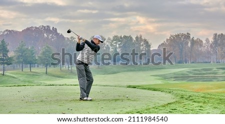 Golfer on a golf course in winter with fog and frost, on the starting tee. Golfer with golf club hitting the ball for the perfect shot.