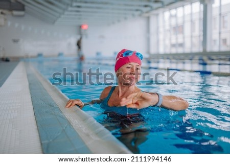 Senior woman looking at smartwatch when swimming in indoors swimming pool. Royalty-Free Stock Photo #2111994146