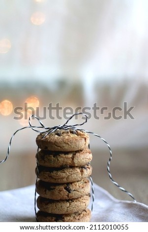 Stack of chocolate chip cookies, tied with ribbon. Lit candle and bokeh lights in the background. Selective focus.