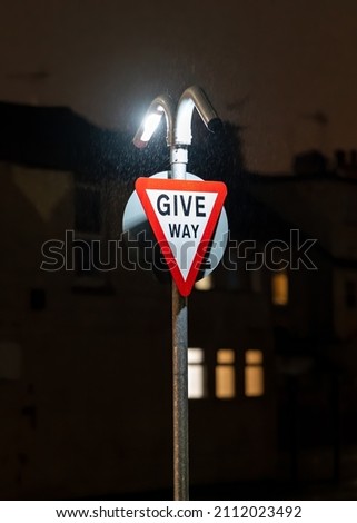 Give way traffic sign brightly illuminated at night in dark. LED lights shining on triangle signage warning traffic of bust junction in darkness.