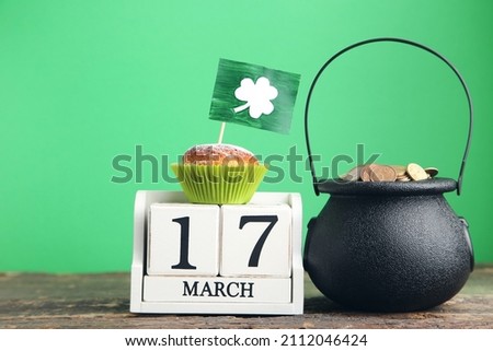 Pot of coins with cupcakes and pictures of clover leaf on green background