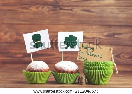 Cupcakes, flags with picture of hat and clover leaf and tag wth text Happy St. Patrick's Day on wooden background