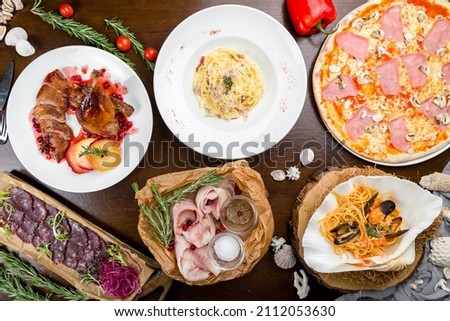 Pizza with ham and mushrooms, pasta with seafood, duck leg confit, sliced vernison, stroganina, pasta carbonara top view on wooden table