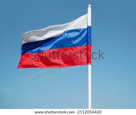 Russian tricolor flag waving in the wind against  sky. Russian flag on blue sky background Royalty-Free Stock Photo #2112056420