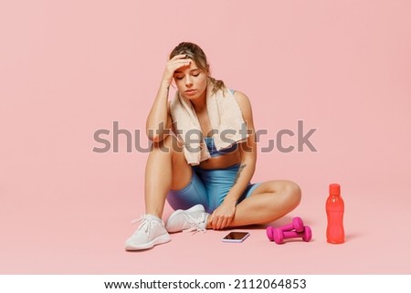 Full body young strong sporty athletic fitness trainer instructor woman wear blue tracksuit spend time in home gym sit on floor hold head isolated on plain light pink background. Workout sport concept Royalty-Free Stock Photo #2112064853