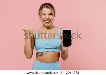 Young sporty athletic fitness trainer instructor woman wear tracksuit spend time in home gym hold mobile cell phone blank screen area do winner gesture isolated on plain pink background Sport concept