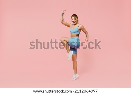 Full body young strong sporty athletic fitness trainer instructor woman wear blue tracksuit spend time in home gym do winner gesture isolated on pastel plain pink background. Workout sport concept.