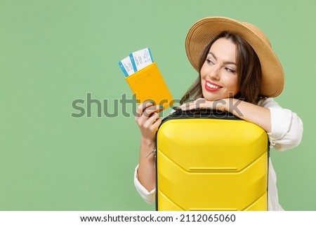 Close up dreamful fun tourist woman in casual clothes hat hold passport tickets yellow suitcase valise isolated on green background Passenger travel abroad weekend getaway Air flight journey concept. Royalty-Free Stock Photo #2112065060