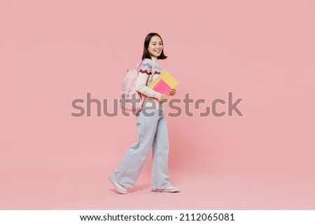 Full body side view teen fun student girl of Asian ethnicity wearing sweater hold backpack books walk going look aside isolated on pastel plain pink background Education in university college concept