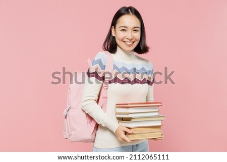 Smiling happy fun teen student girl of Asian ethnicity wearing sweater backpack hold pile of books look camera isolated on pastel plain light pink background Education in university college concept Royalty-Free Stock Photo #2112065111
