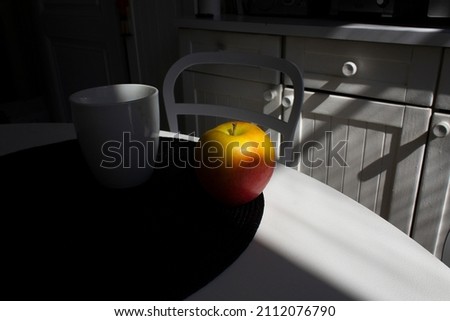 Yellow apple with cup on coffee on white kitchen table with dark shadow 