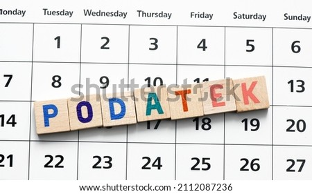 "Podatek" translated as "Tax"  word composed of wooden letters on a piece of paper of the calendar. It's time to settle accounts with the office. Royalty-Free Stock Photo #2112087236