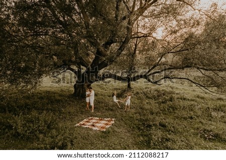 cheerful happy family dad mom daughters have fun playing at summer outdoors together. father mother sisters ride each other on rope swing parents hugging whirl kissing. aerial top under big tree