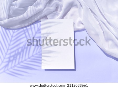Summer tropical stationery still life scene with empty blank wedding card, silk fabric on lilac background. Elegant modern mockup flat lay, harsh palm shadows. Copyspace.