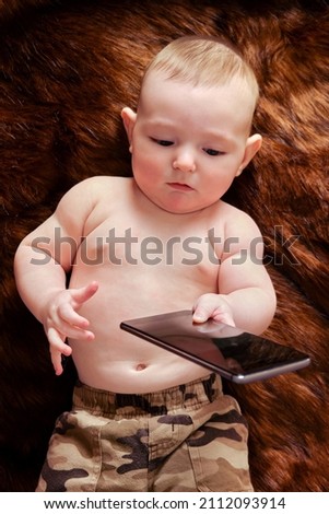 Funny surprised baby boy with a phone in his hands on a fur carpet. Curious child holds a smartphone, top view
