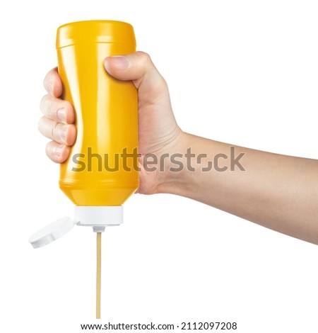 Hand squeezing mustard out of a plastic bottle, isolated on white background Royalty-Free Stock Photo #2112097208