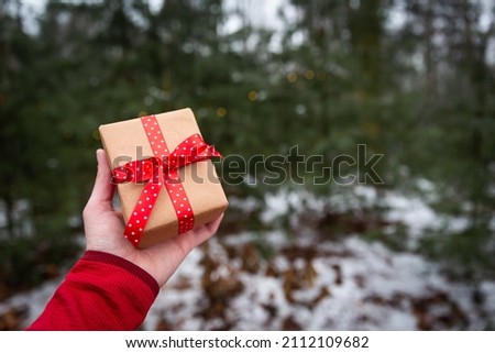 Womans hand holding present wraped in natural brown paper with red dotted ribbon 