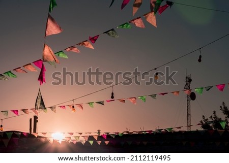 A set of multicolored pennants hanging above the backyard of a home with a dramatic sunset sky as the background.