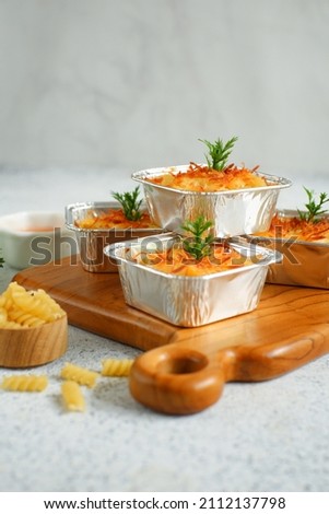 selective focus of baked macaroni schotel in aluminium foil cup on a wooden cutting board against white background