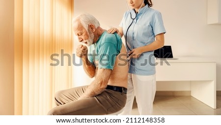 A sick old man coughing and getting medical attention by a female doctor in doctor's office. Heath care, medical support and medical service. Royalty-Free Stock Photo #2112148358