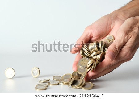 man's hand dropping pile of moving coins on white background