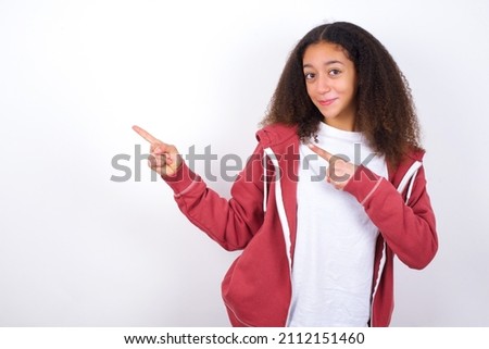 Beautiful teen girl wearing pink jacket against white indicating finger empty space showing best low prices, looking at the camera