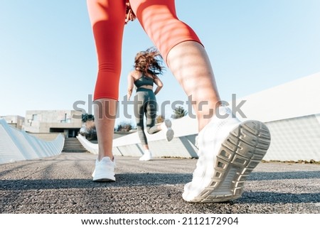 Low angle image of two young sporty girls running fast while working out training. Slim body fitness concept. Bright image, colorful tones. Motion image training outdoors urban zone concept. Royalty-Free Stock Photo #2112172904