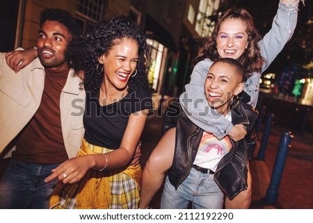 Young people laughing and living their best lives in the city. Happy young people having fun while hanging out together at night. Vibrant friends spending their weekend together. Royalty-Free Stock Photo #2112192290