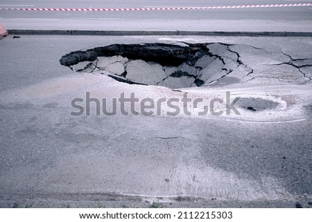 A large pit in the asphalt due to a pipeline accident. A hole in the ground in the middle of the road. Asphalt that has collapsed underground