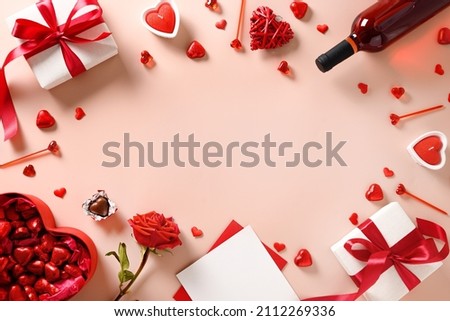 Valentine's day greeting card with red wine, gift, hearts chocolate sweets and red roses on pink background. View from above. Space for your greetings.