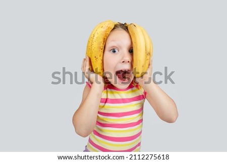 Cheerful little girl with banana poses positively in studio