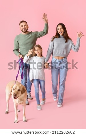 Happy parents with little daughter and Labrador dog on pink background