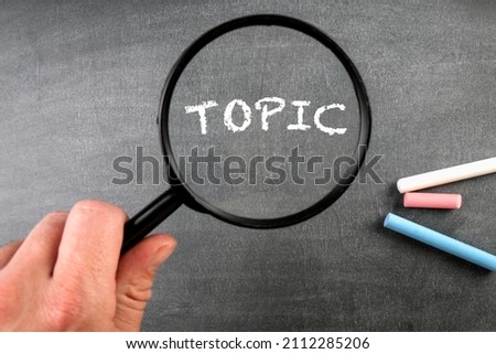 TOPIC. Text and magnifying glass on a black chalkboard.