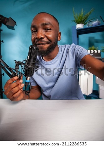 Portrait of smiling social media content creator taking wide angle selfie in online radio studio talking close into professional microphone. Pov shot of famous influencer holding boom arm with mic.