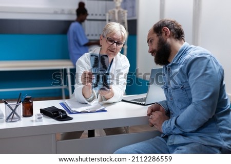 Medic holding x ray scan results for sick patient at checkup visit, explaining diagnosis and disease. Woman doctor analyzing radiography with man, giving medical addvice and support.