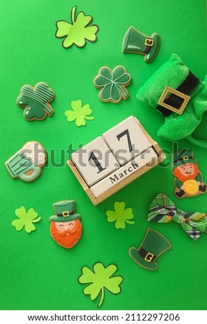 Composition with tasty gingerbread cookies for St. Patrick's Day celebration and calendar on green background