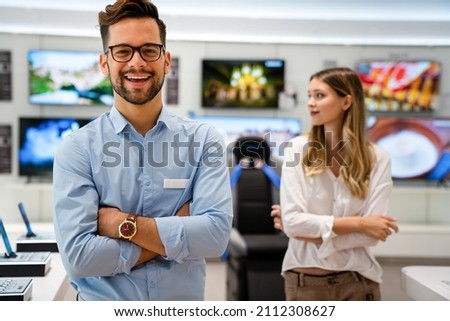 Happy seller man helping to woman to buy a new digital smart device in tech store. Royalty-Free Stock Photo #2112308627