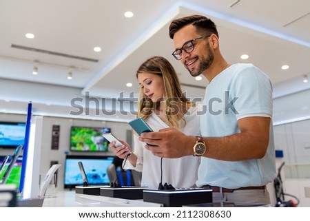 Tech shopping device gadget concept. Happy young people buying a new smartphone in mobile shop. Royalty-Free Stock Photo #2112308630