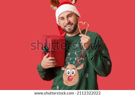 Handsome man with Christmas gift and candy canes on color background