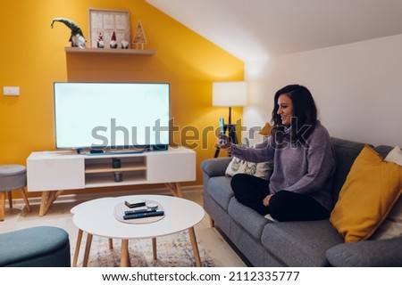 Smiling young hispanic woman sit on sofa at home and using a smartphone for a video call. Digital online communication. Cozy home.