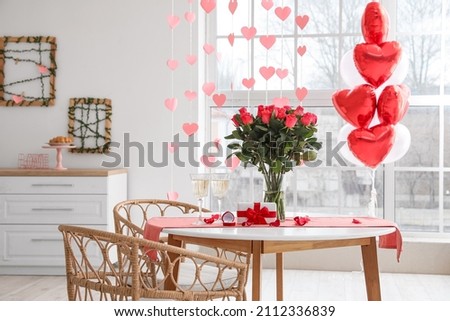 Glasses of champagne, engagement ring and flowers on dining table in room decorated for Valentine's day