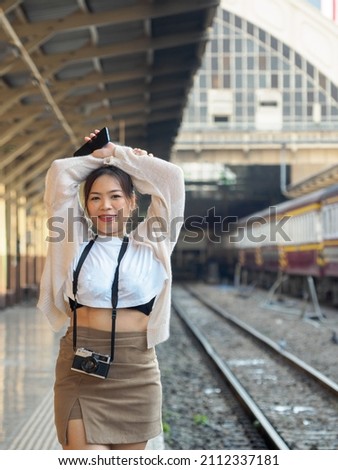 Portrait photography Asian woman beautiful cool long hair wearing white shirt model with retro film camera Standing at the train station (Bangkok), traveling on vacation during the evening of the day.
