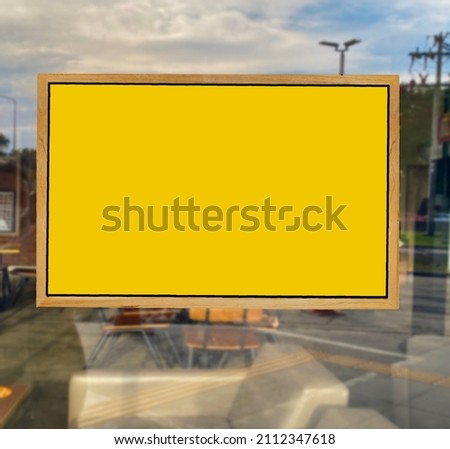 Blank yellow sign on wooden frame with copyspace for your design hanging  in front of a window door of a restaurant, shop, office or other 